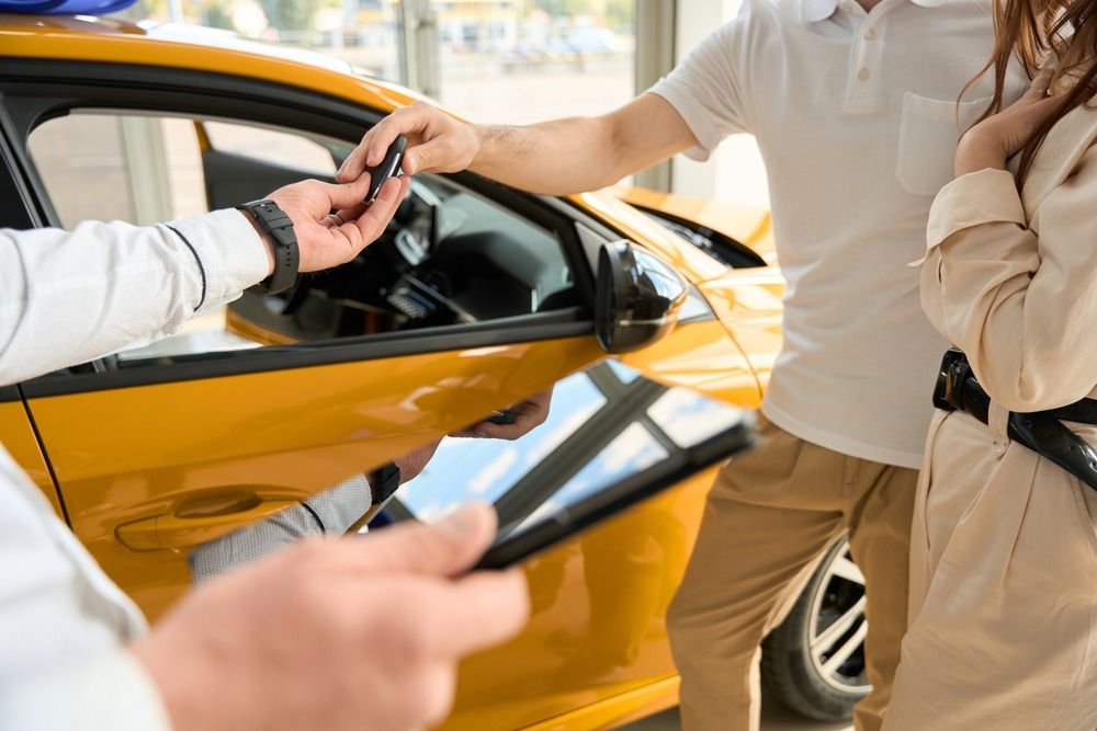 perito entrega llaves de coche a pareja con vehiculo amarillo de fondo